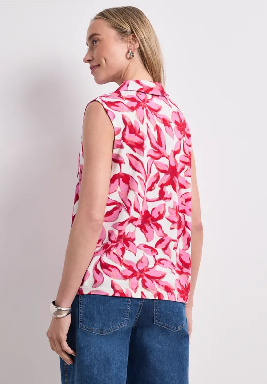 Femme de dos portant un haut sans manches à motif floral rose et blanc avec un jean.