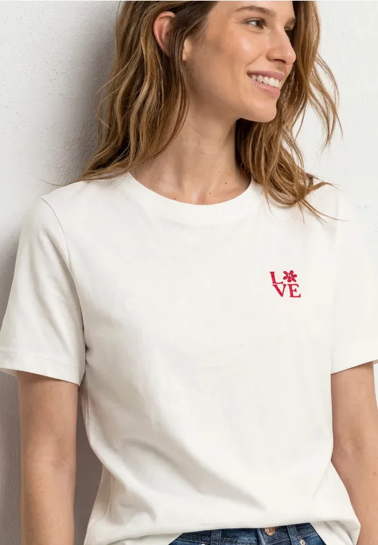 Frau trägt ein schlichtes weißes T-Shirt mit kleinem roten Schriftzug 'LOVE' auf der Brust.