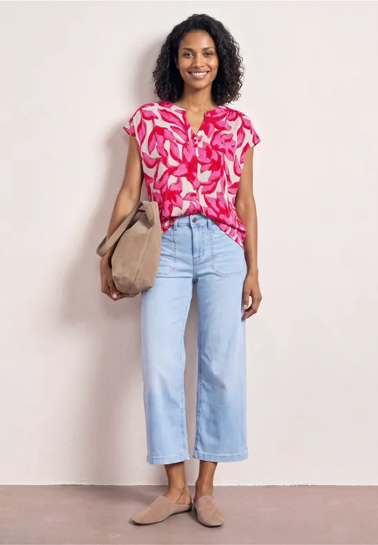 Femme portant un chemisier rose à motifs, un jean large clair, un sac beige et des mocassins.