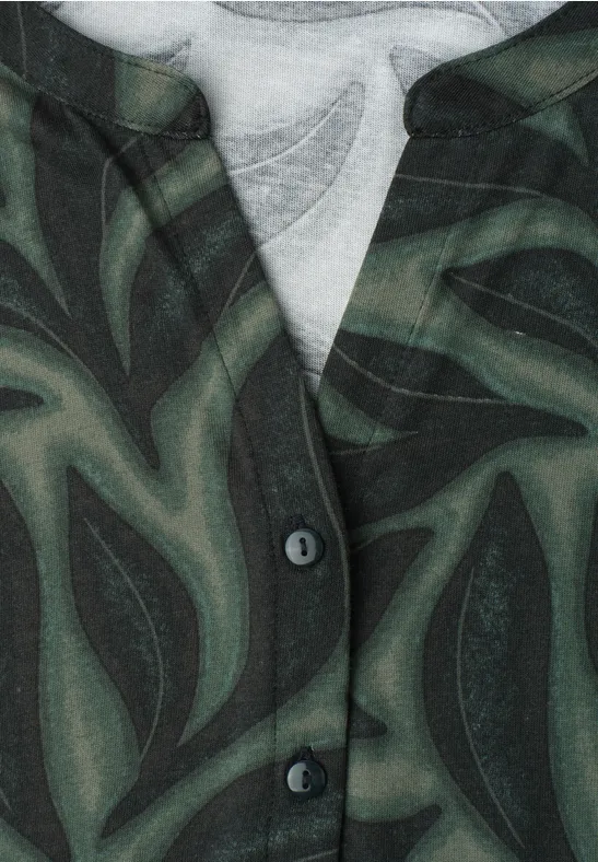 Gros plan sur une chemise à motif de feuilles vert foncé et deux boutons.