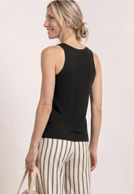 Eine Frau von hinten in schwarzem ärmellosem Top, gestreifter weißer Hose und Strohtasche.