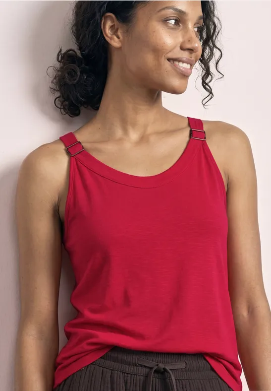 Vrouw in rood mouwloos shirt en donkere broek, frontaal, gezicht onscherp.