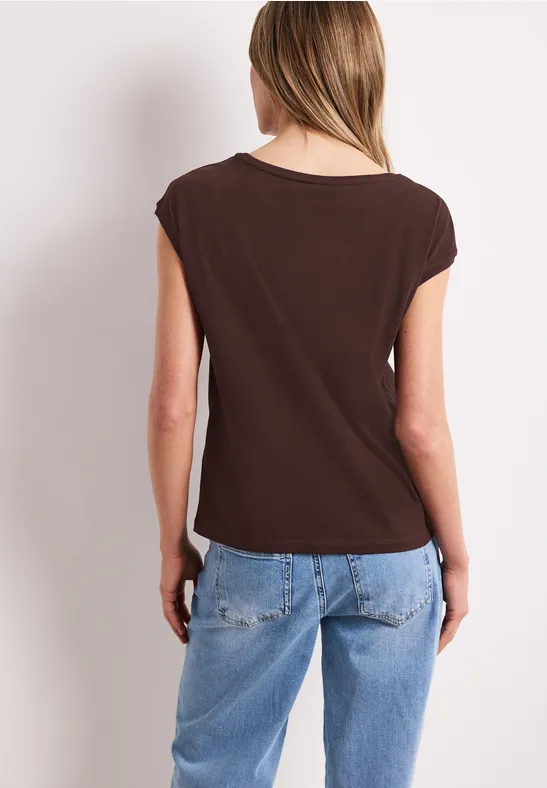 Vrouw van achteren in een bruin shirt en lichtblauwe jeans voor een witte achtergrond.
