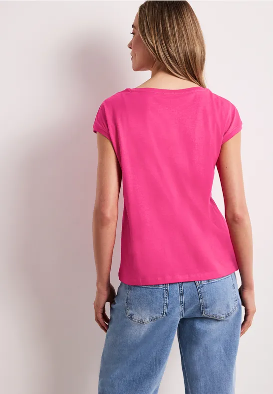 Eine Frau von hinten in pinkem T-Shirt und blauen Jeans.