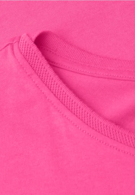 Nahaufnahme eines pinkfarbenen T-Shirt-Ausschnitts mit sichtbarer Naht und weichem Baumwollstoff.