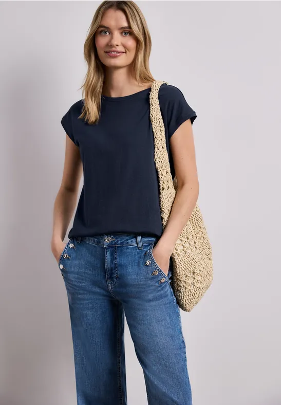 Vrouw in donkerblauw T-shirt en losse spijkerbroek, met gehaakte schoudertas.