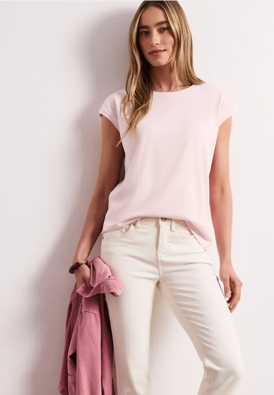 Femme en t-shirt rose pâle et pantalon clair, tenant une veste rose