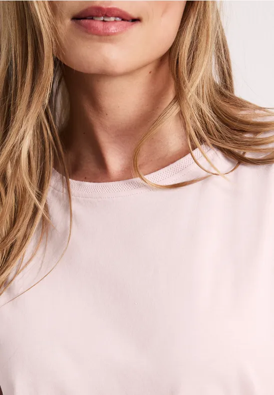 Gros plan sur une femme blonde portant un T-shirt rose, seuls le cou et les lèvres sont visibles.