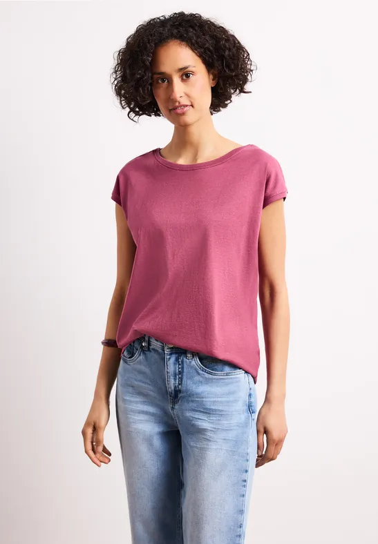 Person mit rosa T-Shirt und blauen Jeans vor weißem Hintergrund.