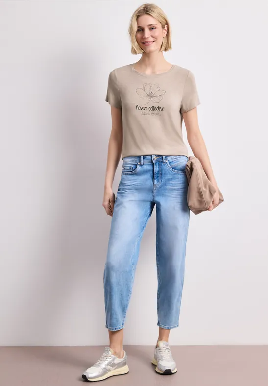 Femme décontractée portant un t-shirt, jean clair, baskets et pochette.