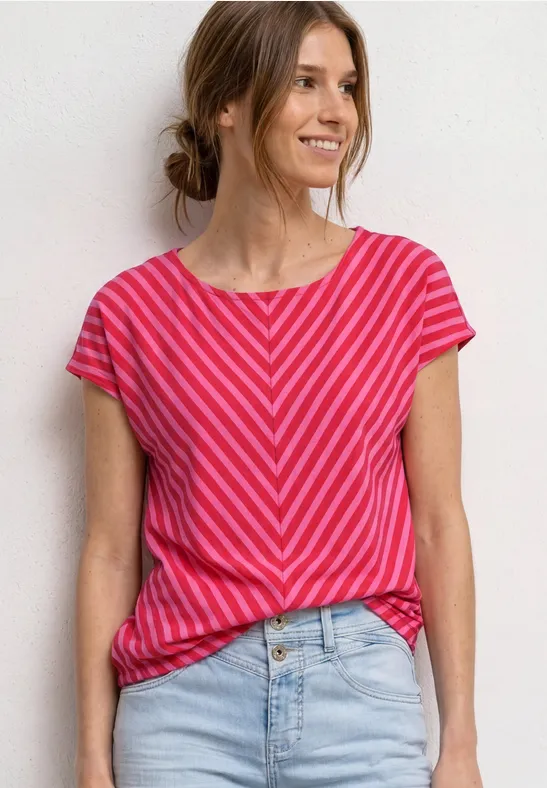 Frau trägt pink-rot gestreiftes T-Shirt und Jeans vor weißem Hintergrund.
