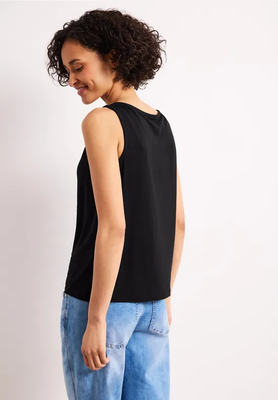 Frau von hinten in schwarzem ärmellosem Top und blauer Jeanshose, Gesicht unscharf.