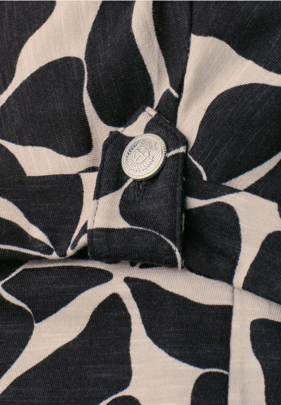 Close-up van donkerblauw-beige stof met groot bloemmotief en een zilverkleurige knoop.
