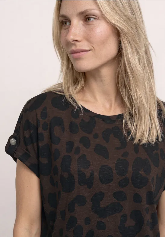 Vrouw met halflang blond haar draagt een bruin-zwart shirt met korte mouwen en luipaardprint.