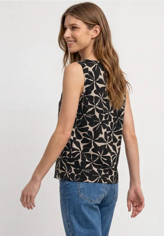 Vrouw van achteren in een blauwe spijkerbroek en een zwarte mouwloze top met wit geometrisch patroon.