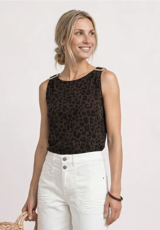 Frau im ärmellosen, braun-schwarzen Leoparden-Top und weißen Jeans, Haare im lockeren Dutt.