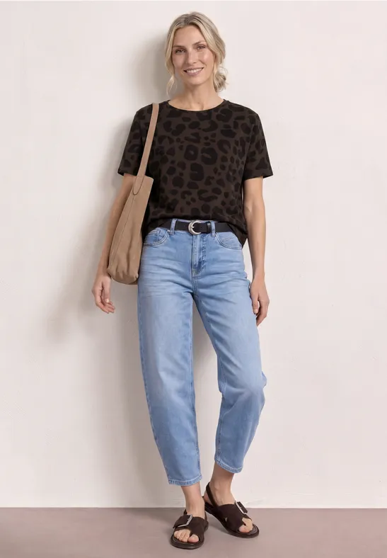 Personne devant un mur blanc porte un t-shirt léopard noir, jean clair, sandales noires et tote bag.