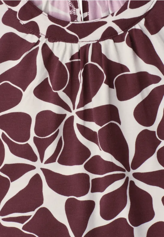 Close-up van een bordeaux T-shirt met witte bloemprint in organische vormen.