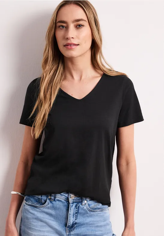 Frau in schwarzem V-Ausschnitt-T-Shirt und blauen Jeans vor weißem Hintergrund.