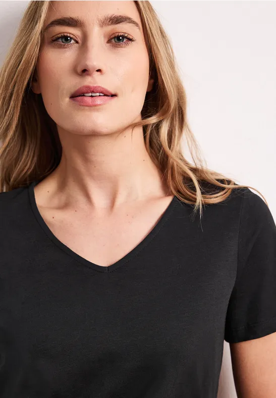 Porträt einer jungen Frau in schwarzem V-Ausschnitt-Shirt, leichte Wellen im Haar, helle Studio-Umgebung.