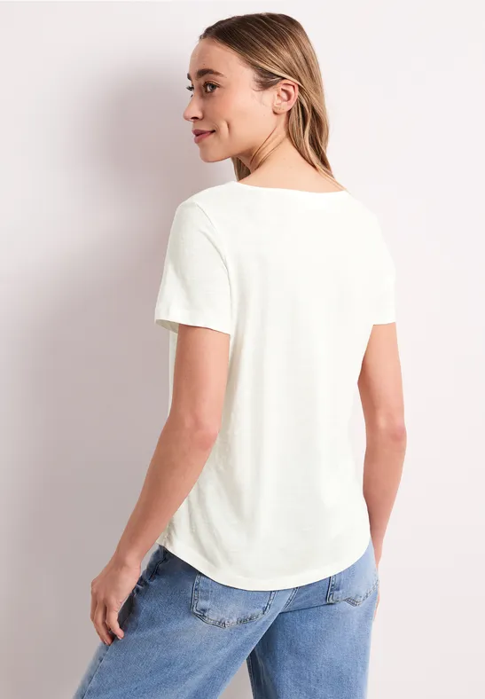 Rückansicht einer Person mit weißem T-Shirt und blauer Jeans vor neutralem Hintergrund.