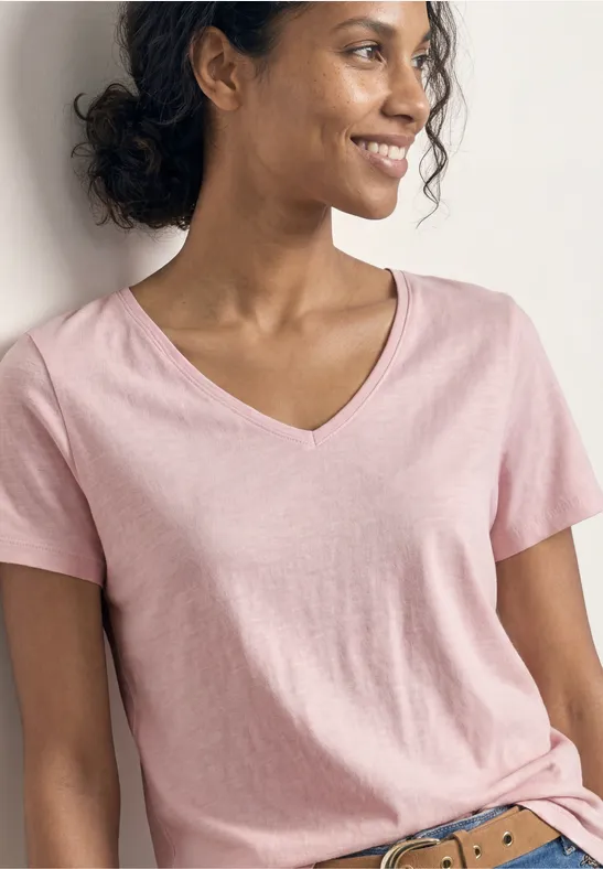 Vrouw in een roze V-hals T-shirt voor een neutrale achtergrond, gezicht onscherp, zicht van hals tot heup.