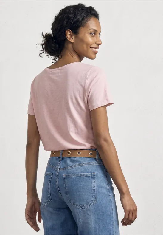 Vrouw van achteren in een roze t-shirt en blauwe spijkerbroek met leren riem.