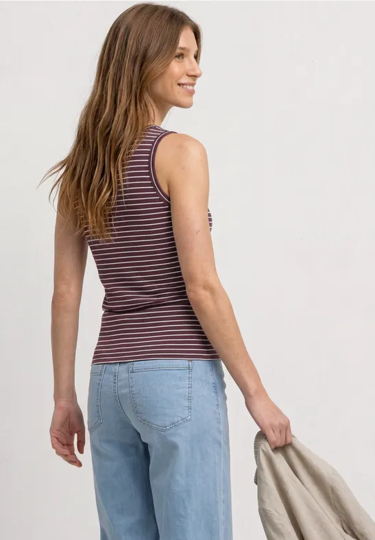 Een vrouw van achteren met een gestreept topje, een blauwe jeans en een beige jas in haar hand.