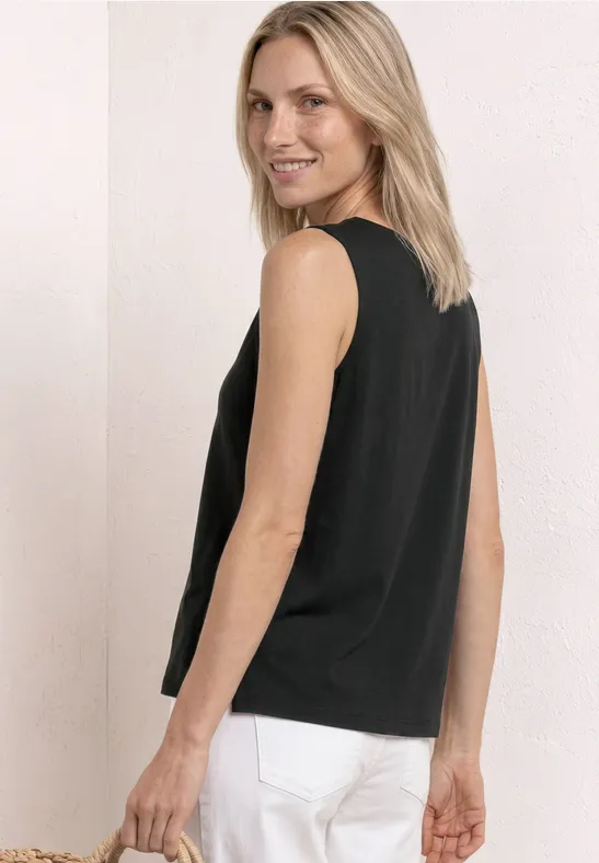 Person in schwarzem ärmellosem Top und weißen Hosen, seitlich abgewandt.