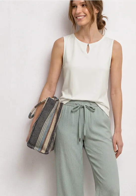 Vrouw in mouwloos wit topje en mintgroene broek met tunnelkoord, met gestreepte tas over de schouder.