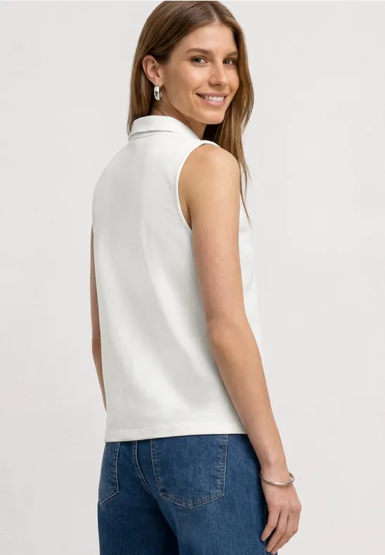 Frau in weißem ärmellosen Poloshirt mit Stehkragen und blauen Jeans, seitliche Rückansicht.