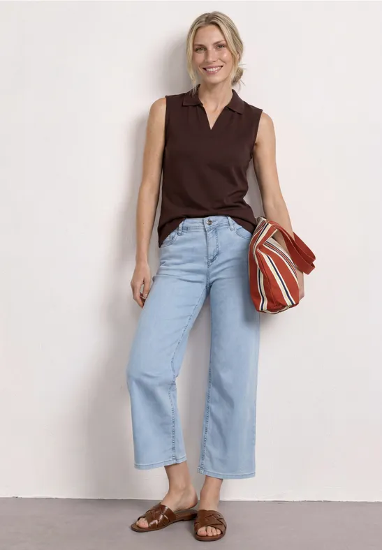 Frau in dunkelbraunem ärmellosem Oberteil, hellblauen Culotte-Jeans, braunen Sandalen und gestreifter Tasche.