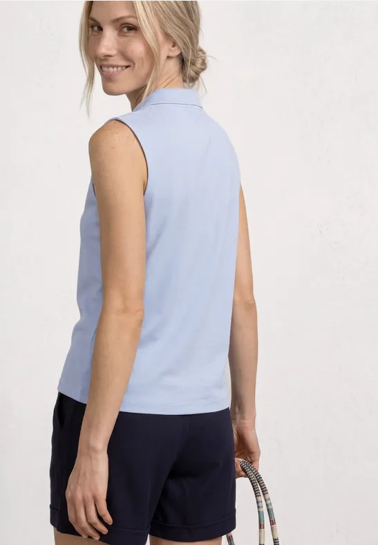 Femme de dos en haut bleu clair sans manches, short foncé et sac à la main.