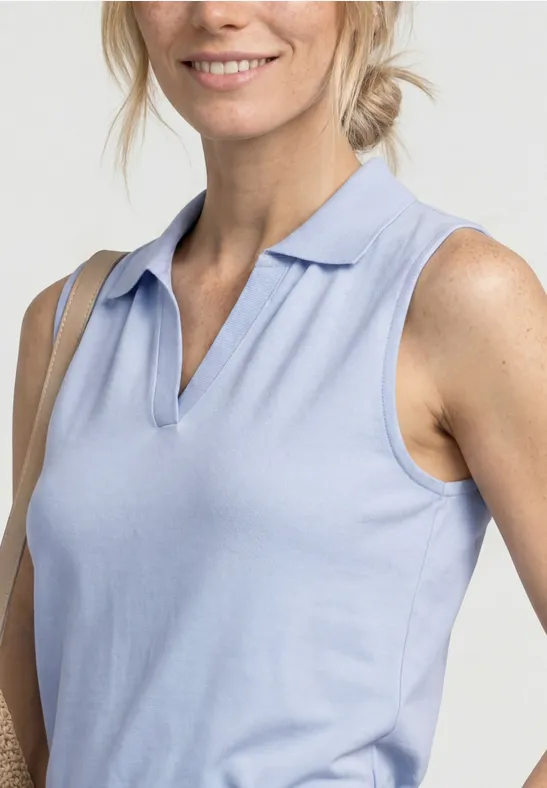 Gros plan d'une femme souriante portant un polo sans manches bleu clair, épaules et buste visibles.