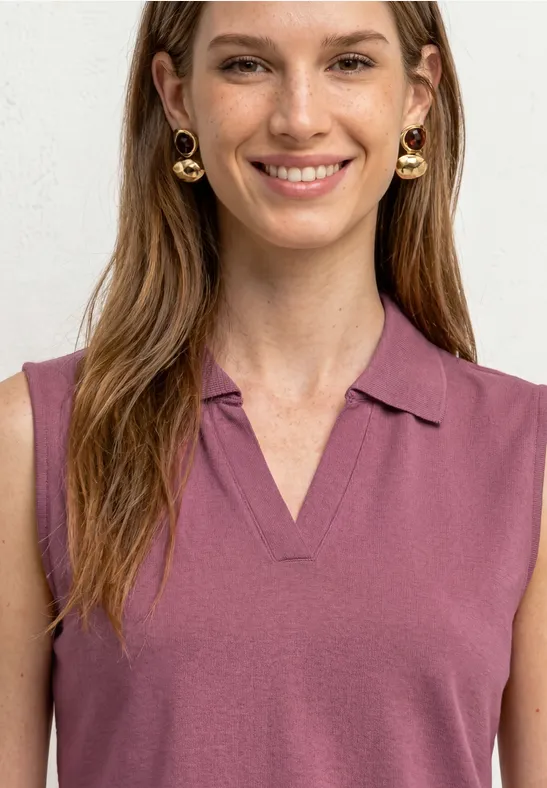Een vrouw met lang bruin haar draagt een mouwloze paarse polo en gouden creolen.