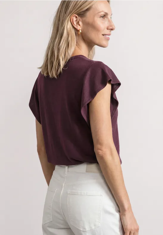 Vrouw van achteren in witte broek en paarse top met gerimpelde mouwen