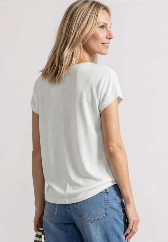 Rückenansicht einer Frau mit blondem Haar, die ein helles T-Shirt und blaue Jeans trägt.