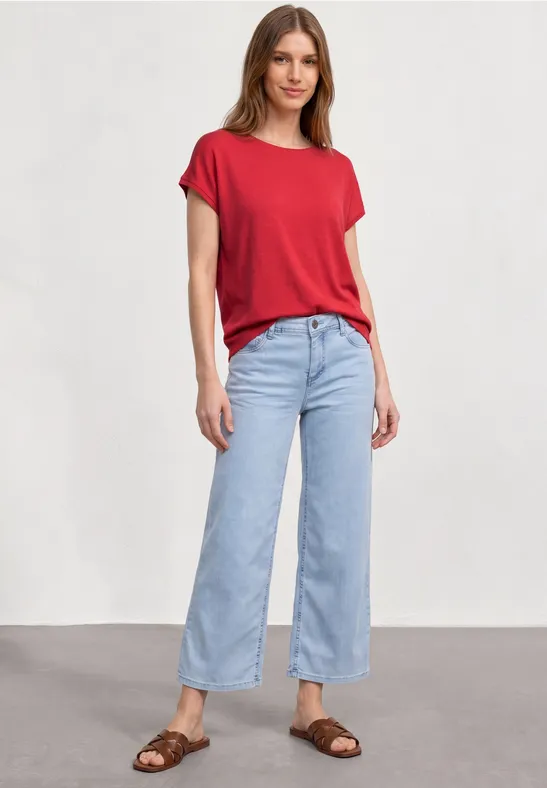 Vrouw in rood T-shirt, lichtblauwe wijde jeans en bruine sandalen.