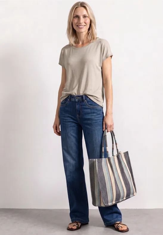 Vrouw in beige T-shirt, blauwe jeans en zwarte schoenen met gestreepte shopper.