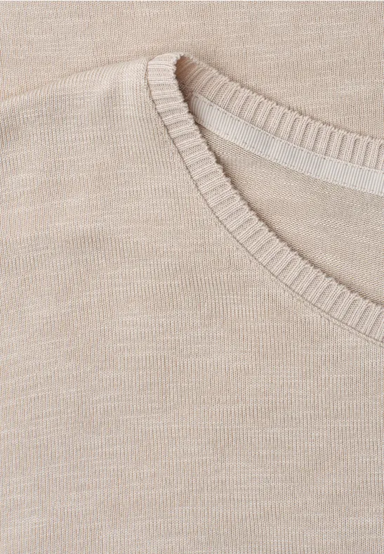 Close-up van de halslijn van een beige gebreide trui.