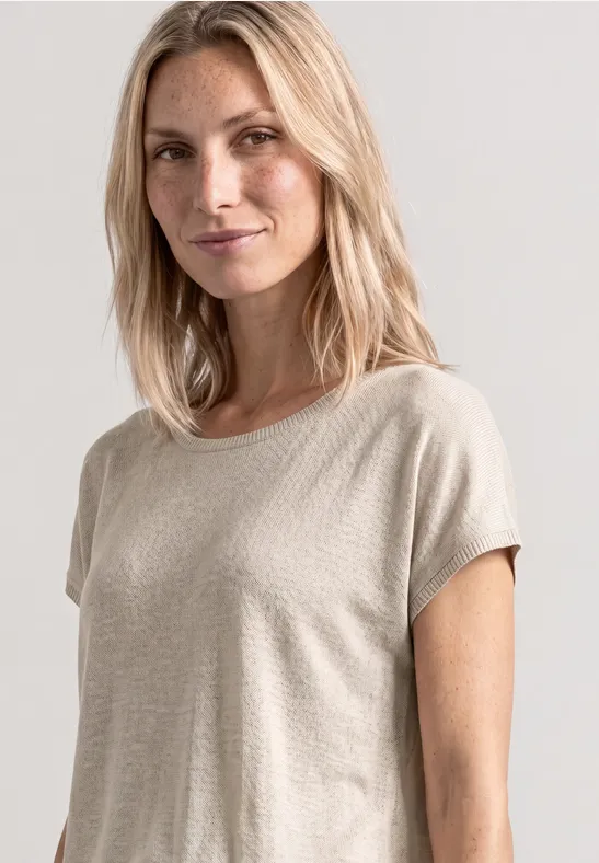 Vrouw in beige T-shirt met halflang blond haar voor een neutrale lichtgrijze achtergrond.