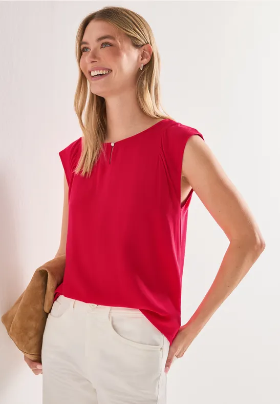 Vrouw met rood mouwloos shirt en witte broek, met een bruine tas.