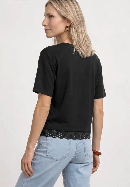 Frau von hinten mit schulterlangem blondem Haar, schwarzem T-Shirt mit Spitze und hellblauer Jeans