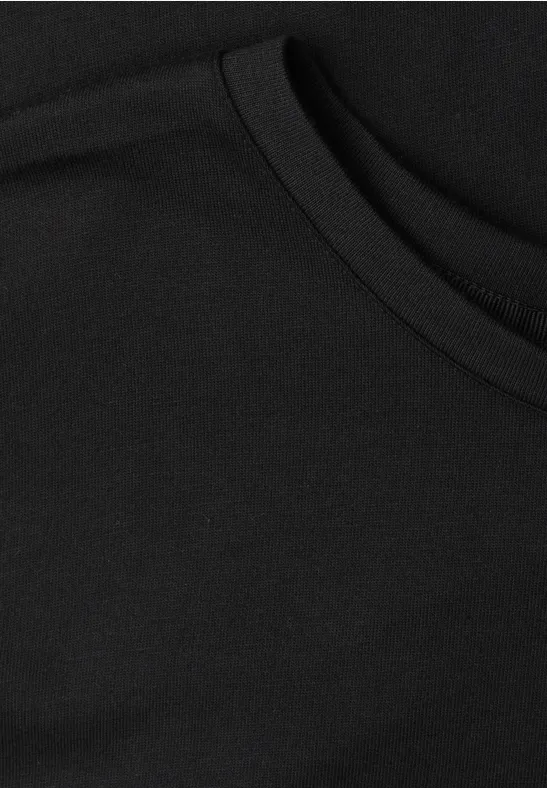 Schwarzer Stoff mit abgerundetem Tascheneingriff, vermutlich eine Brusttasche an einem T-Shirt.