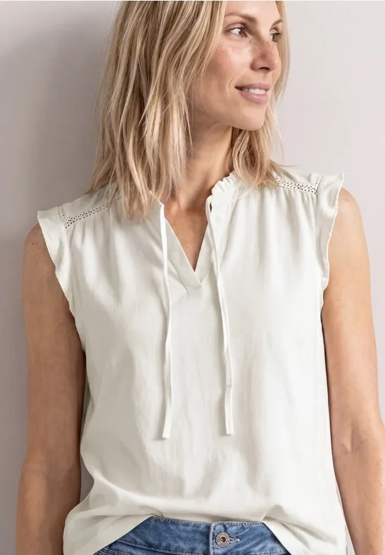 Vrouw draagt mouwloze witte blouse met V-hals en bindbandjes.
