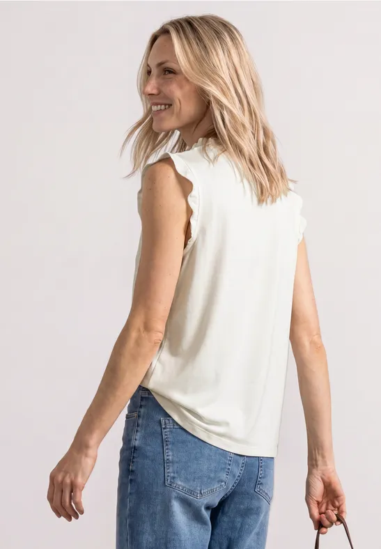 Vrouw van achteren gezien met blond haar, draagt een mouwloos wit topje, spijkerbroek en houdt een donkere clutch.