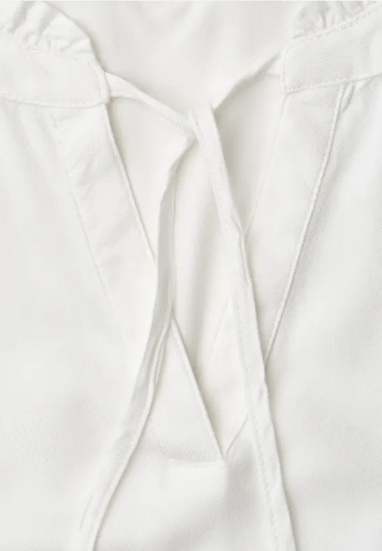 Close-up van een wit bovenstuk met V-hals en decoratieve linten