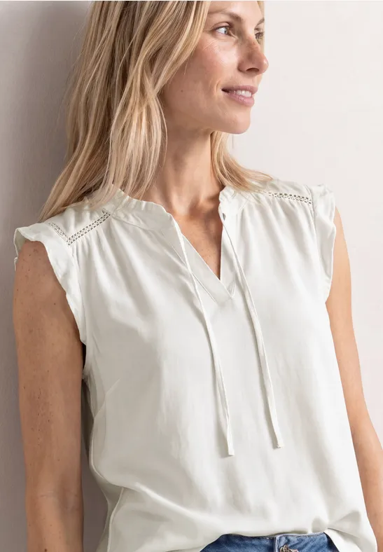 Mouwloze witte blouse met V-hals, fijne kanten details op de schouders en tunnelkoordjes.