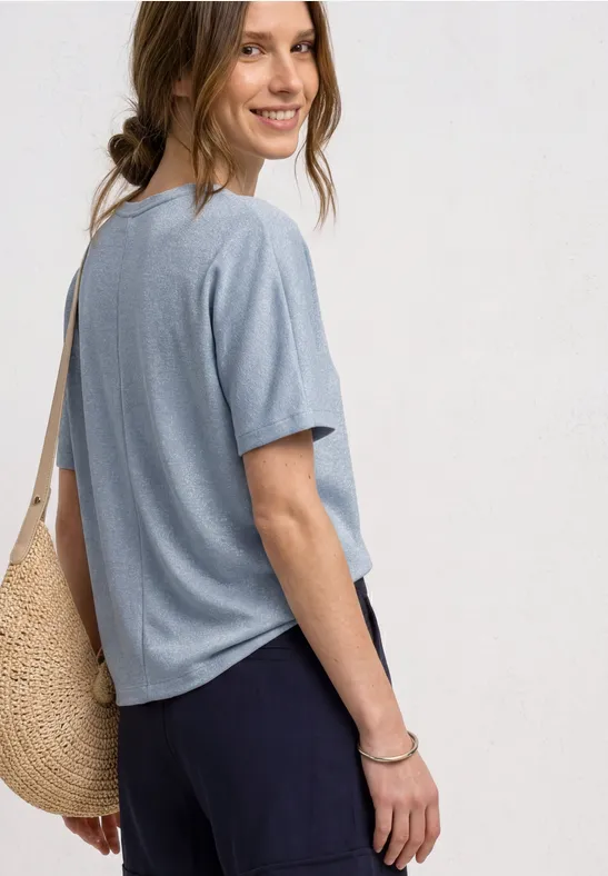Une personne vue de dos porte un t-shirt bleu clair, un pantalon foncé et un sac en paille.