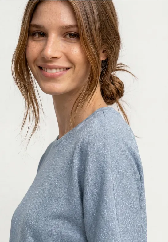 Gros plan d’une femme en pull bleu clair, cheveux noués en chignon décontracté.